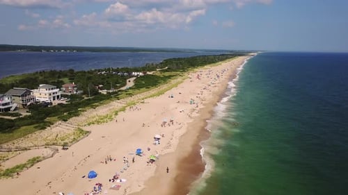 Drone shot of Atlantic Ocean and bay with shore houses, beach, boats, and boardwalk.