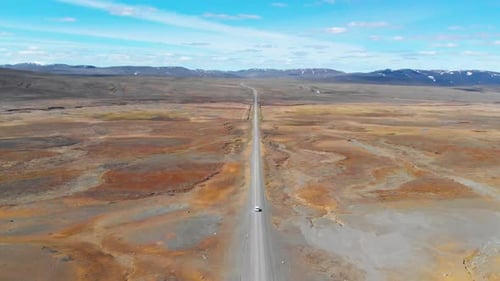 Areal shot of a car travelling across vast dry empty area alone on an endless road.