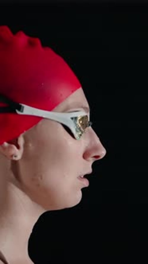 Focused Female Swimmer in Red Swim Cap and Suit Preparing in Profile Against Dark Background