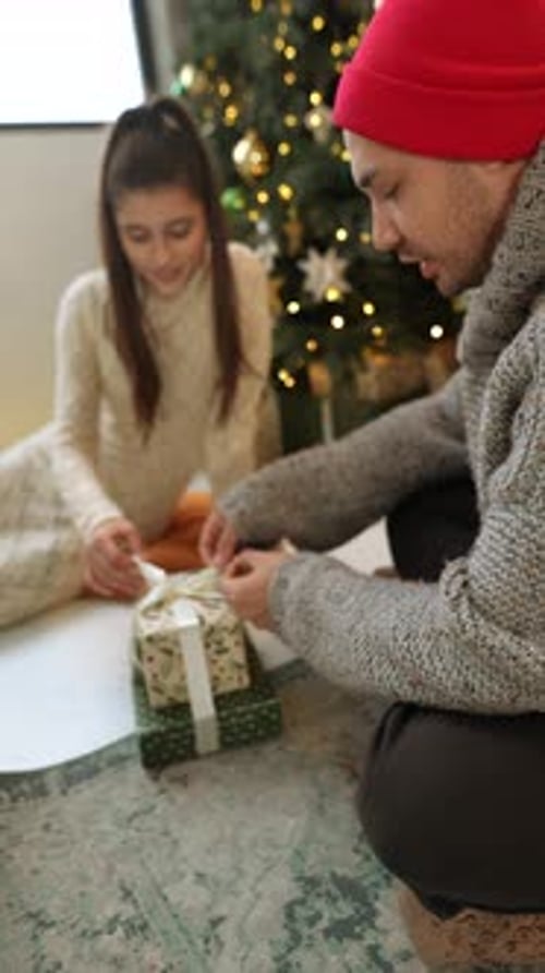 Young Adults Wrapping Christmas Gifts by Tree