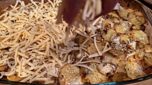 Hand Sprinkling Cheese Over Layered Potato and Ground Beef Casserole Preparation Close-Up