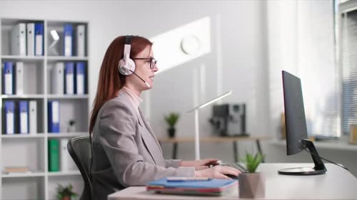Technical Support Charming Young Woman in Glasses Talking to Client Using Headset While Sitting at a