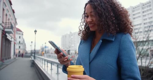 Woman Using Smartphone and Holding Coffee Cup Outdoors