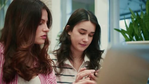 Two Young Women Discussing Work on a Laptop in a Modern Office