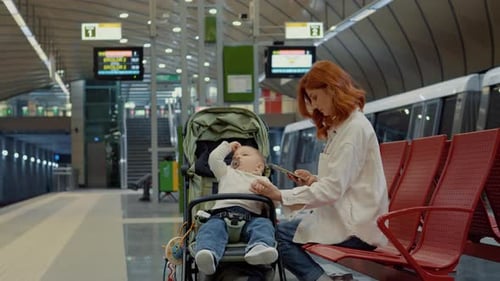 Mother waits on bench with baby for subway while using her phone