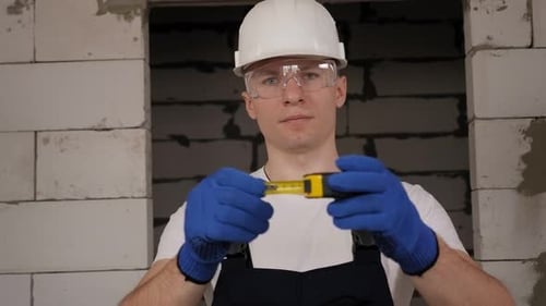 A Construction Worker in a Helmet and Glasses Holding a Measuring Tape Measure