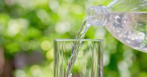 Pouring Purified Water Into Glass From the Bottle on Green Natural Background