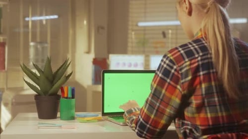 Vista posterior de una mujer joven escribiendo en un teclado de computadora portátil con pantalla verde