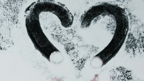 Close-up of a finger drawing on a snow-covered glass surface romantic heart shape