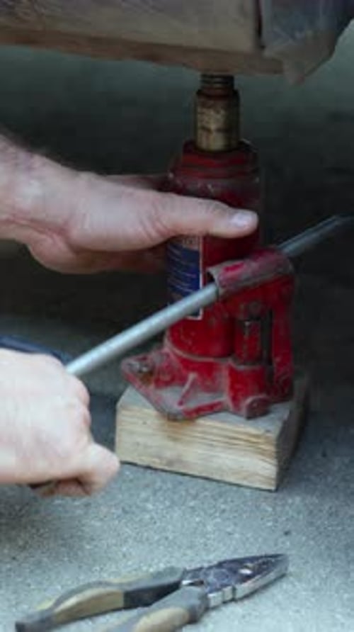 Vertical Footage of a Man Lifts a Car Using a Hydraulic Jack for Essential Wheel Repairs