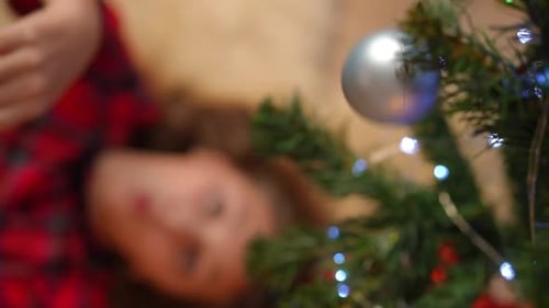 Girl Reaches for Christmas Ornament near Christmas Tree