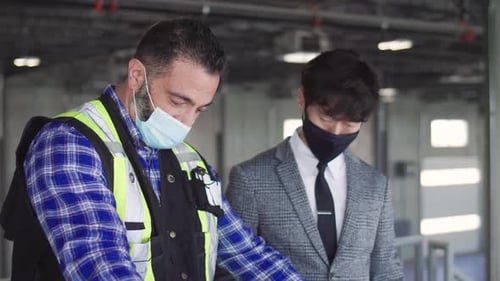 Architect and foreman in face masks discuss blueprints in warehouse