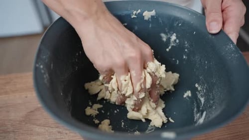 A woman kneads the dough by hand in a blue bowl. Top view, slow motion.