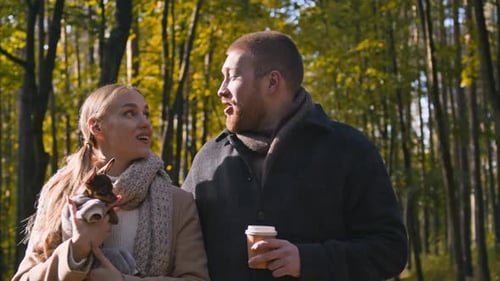 Woman with Dog in Hands Kissing Boyfriend Drinking Coffee Walking in Fall Park