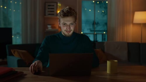 Handsome Smiling Man Works on a Laptop while Sitting at His Desk at Home. Portrait of a Young Freel
