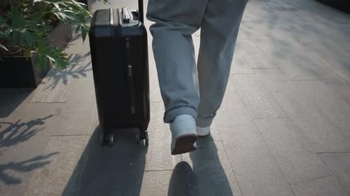 Traveler Pulling Suitcase Along Urban Sidewalk on Sunny Day