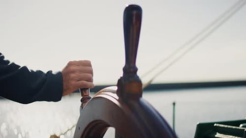 Hand steering wooden ship wheel on traditional sailing vessel under sunlight