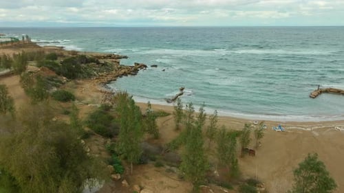 Overhead shot of a coastal village with white houses, blue beach umbrellas, and a curving sandy shor