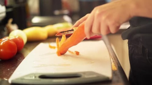 Close up female hands peeling carrots in the kitchen in slow motion