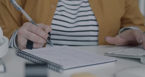 Hands Writing in a Notebook and Typing on Keyboard
