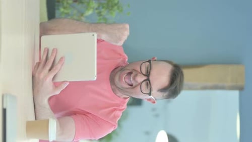 Man Cheers While Using Tablet at Desk Indoors