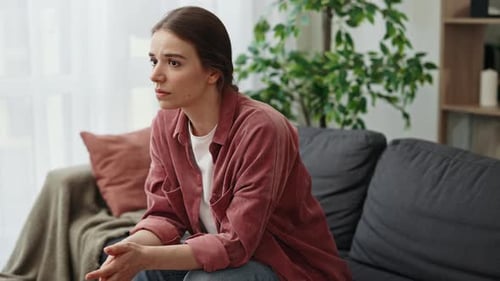 Pensive Young Woman Sitting on Sofa Indoors