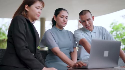 Close-up of three co-worker freelancers sitting at a table with laptops discussing new enterprise