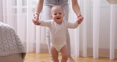 Happy Little Baby Girl Learning to Walk with Mother Help