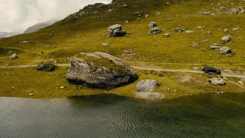 Car Going By Dirt Road Near High Mountain Lake In Alps View From Drone