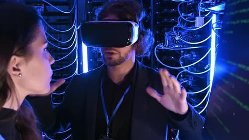 Woman programming in a server room while a man is using a Virtual Reality headset