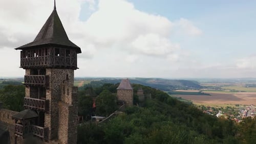 Medieval tower overlooking a landscape with another tower in the distance, under a partly cloudy sky