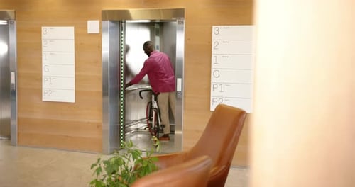 Man in office building elevator holding bicycle, commuting to work