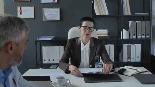 Female Clinical Director Handing Reports to Two Physicians at Meeting in Office