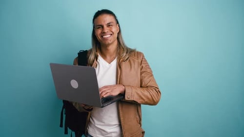 Smiling Young Man Types on Laptop in Studio
