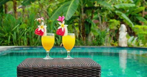 Zwei gelbe Cocktails, Saft mit Blumen, stehen in der Nähe des Pools