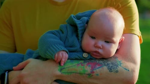 Young Father with His Newborn Baby in the Park on a Sunny Day