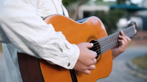 Young Male Artist Walking In The Street While Playing An Acoustic Guitar