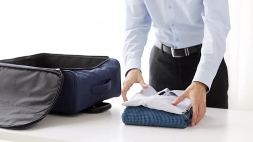 Man Packing Clothes in Suitcase on White Table