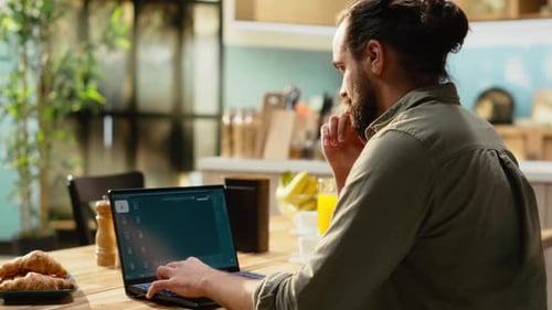 Man Edits Video on Laptop at Breakfast Table