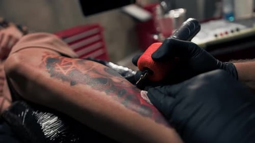 Close-up - the process of tattooing a woman on her leg. Male tattoo artist making a tattoo
