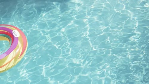 Colourful inflatable ring floating in sunny swimming pool, copy space, slow motion