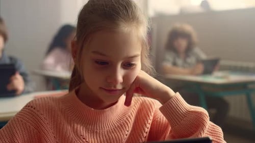 Thoughtful Schoolgirl Looking On Screen Of Digital Tablet During School Lesson. Female Student St...