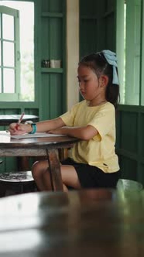 Focused Young Girl Diligently Writing and Drawing at a Rustic Wooden School Desk