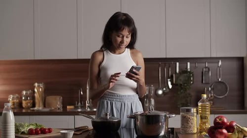 Young Woman Cooking and Using Smartphone in Kitchen