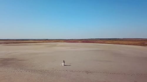 Aerial of Pretty Woman in Gorgeous Wedding Dress Walking at Sandy Desert Landscape of a Dried Lake