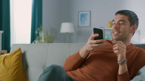 Man Relaxes on Couch Browsing on Smartphone