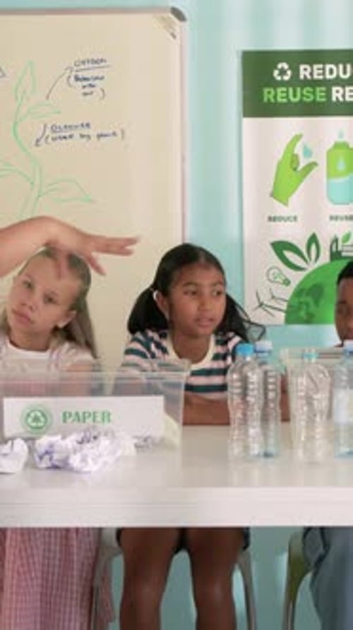 Vertical video: Hearing left prompt kids in tops raising hands in class to reply PAPER-bin bottles