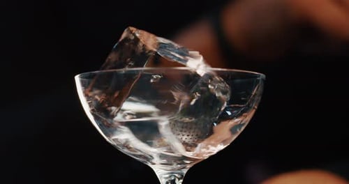 Close up of a bartender is putting professional crystal ice cubes in a glass while preparing an al