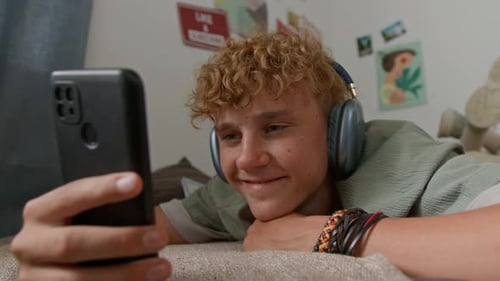 Teenager Lies Down, Watching Phone with Headphones On