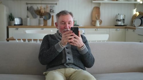 Senior Man Using Smartphone on Sofa at Home